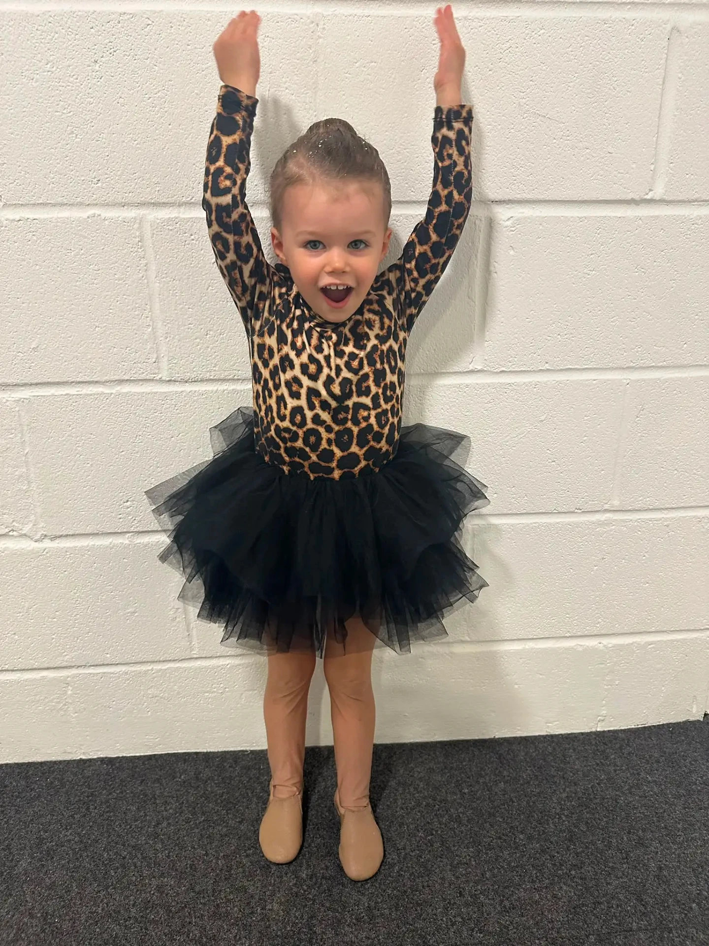 Young dancer in a leopard print leotard and black tutu cheering with arms raised