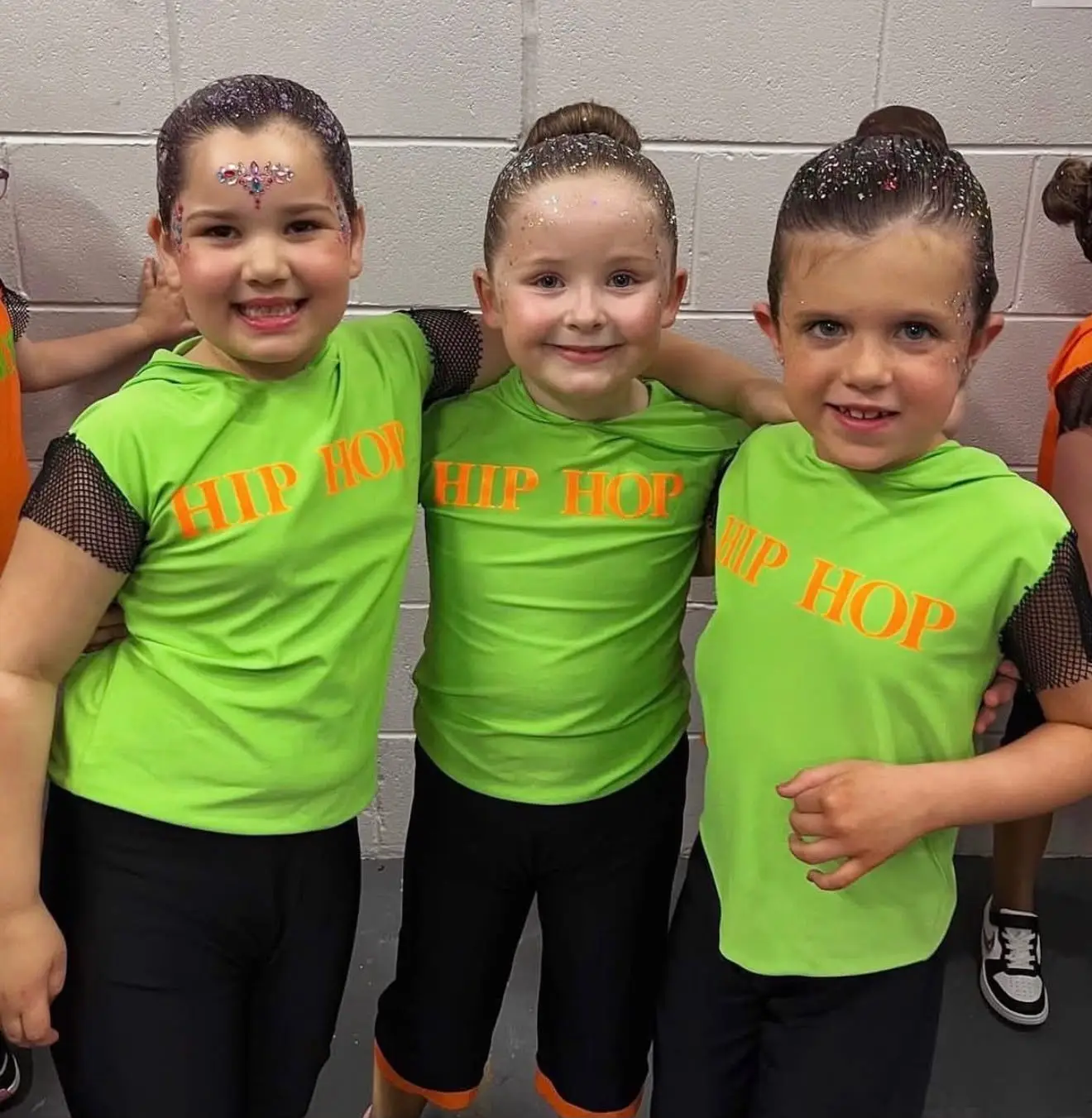 Three girls in neon green hip hop tops smiling together
